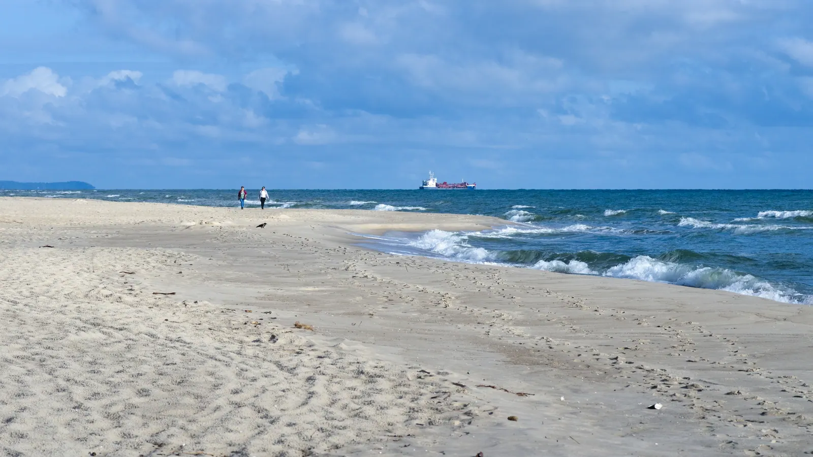 Plaża w Jastarni z jasnym piaskiem, falami i widokiem na Półwysep Helski.