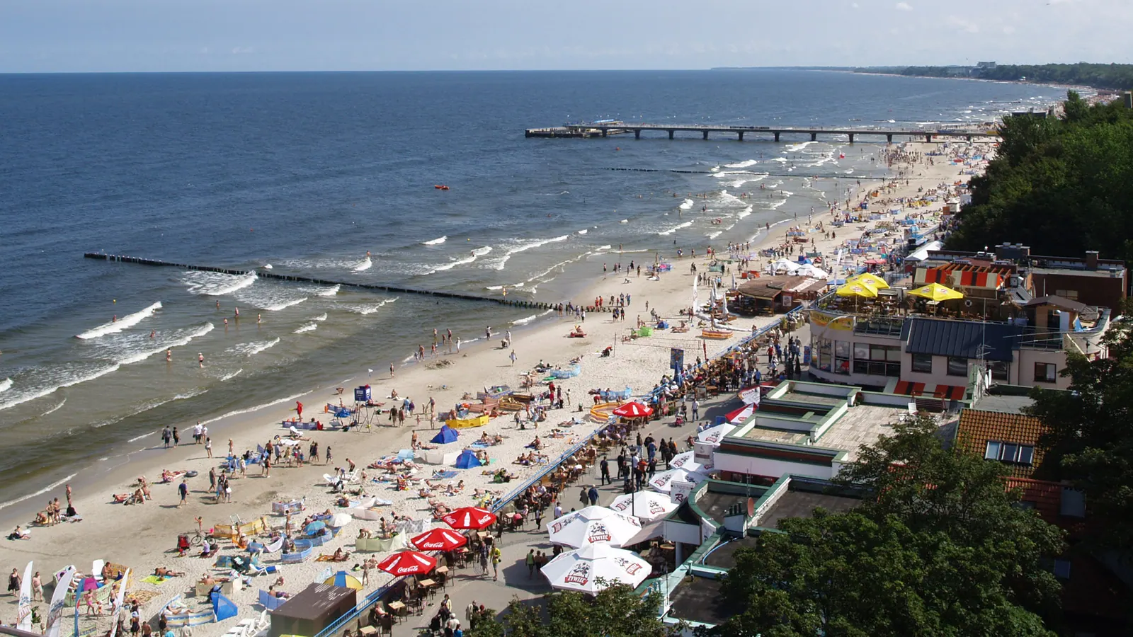 Plaża w Kołobrzegu z widokiem na molo, piasek i zabudowę kurortu.
