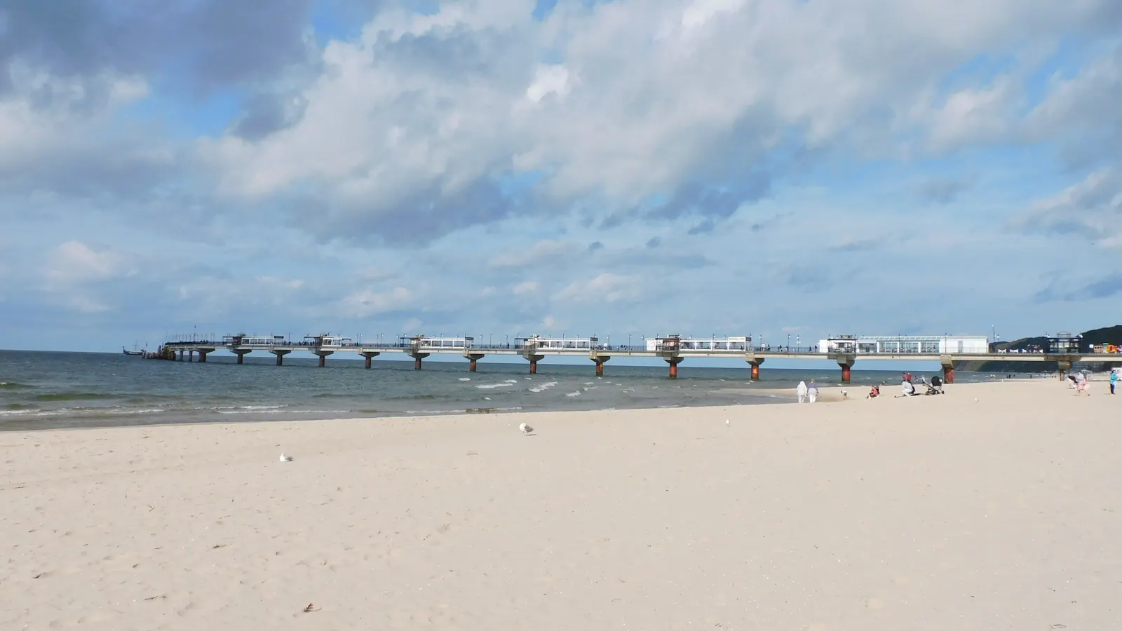 Molo i plaża w Międzyzdrojach z jasnym piaskiem i spokojnym morzem.