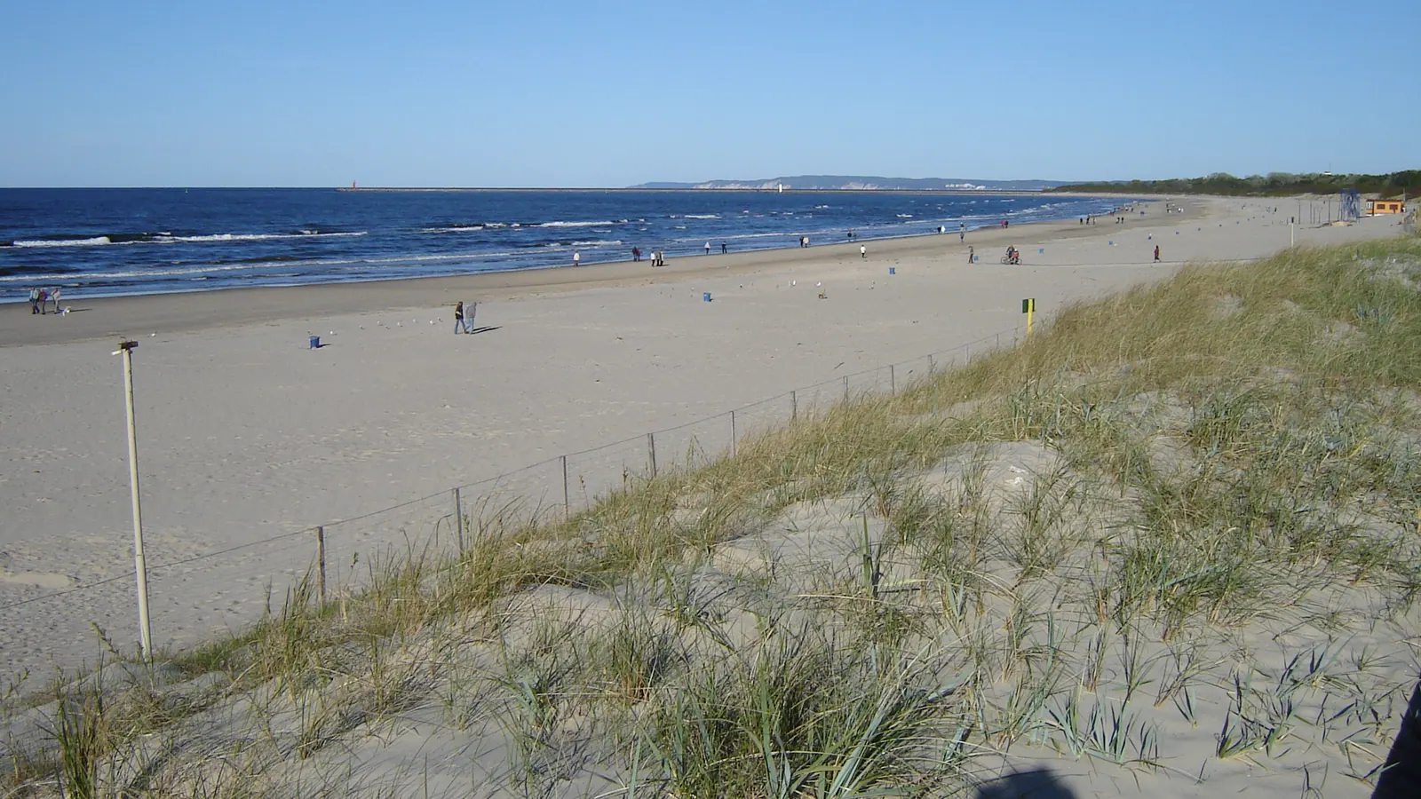 Szeroka piaszczysta plaża w Świnoujściu z wydmami i wejściem na kąpielisko.